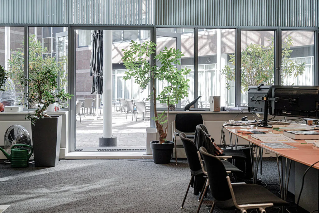 Kantoorruimte aan de Burgemeester van Karnebeeklaan met uitzicht op een binnenterras met tafels, stoelen en planten.